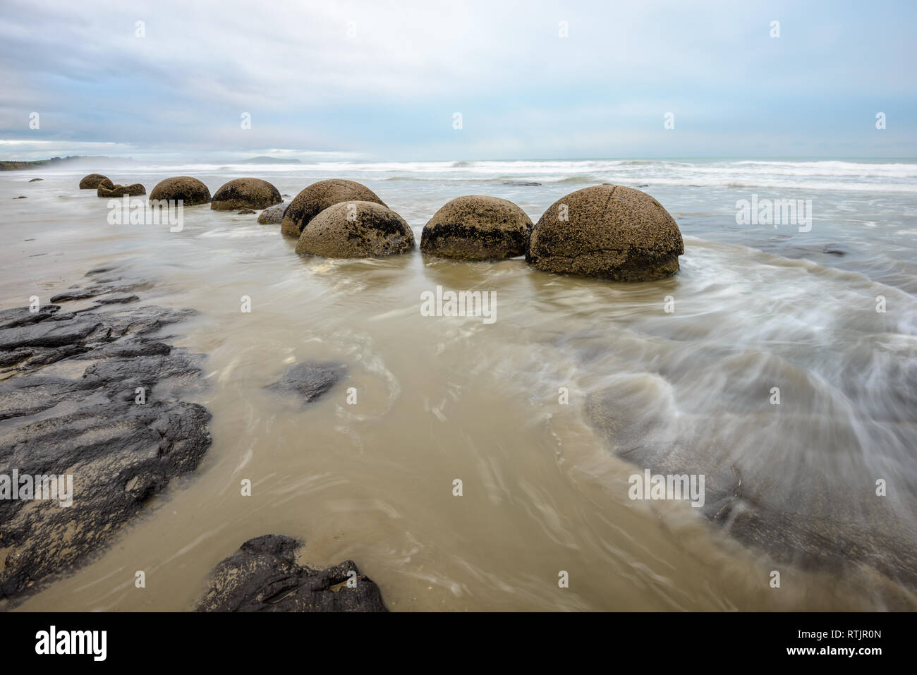 Beeindruckende Moeraki Boulders in den Pazifischen Ozean Wellen Stockfoto