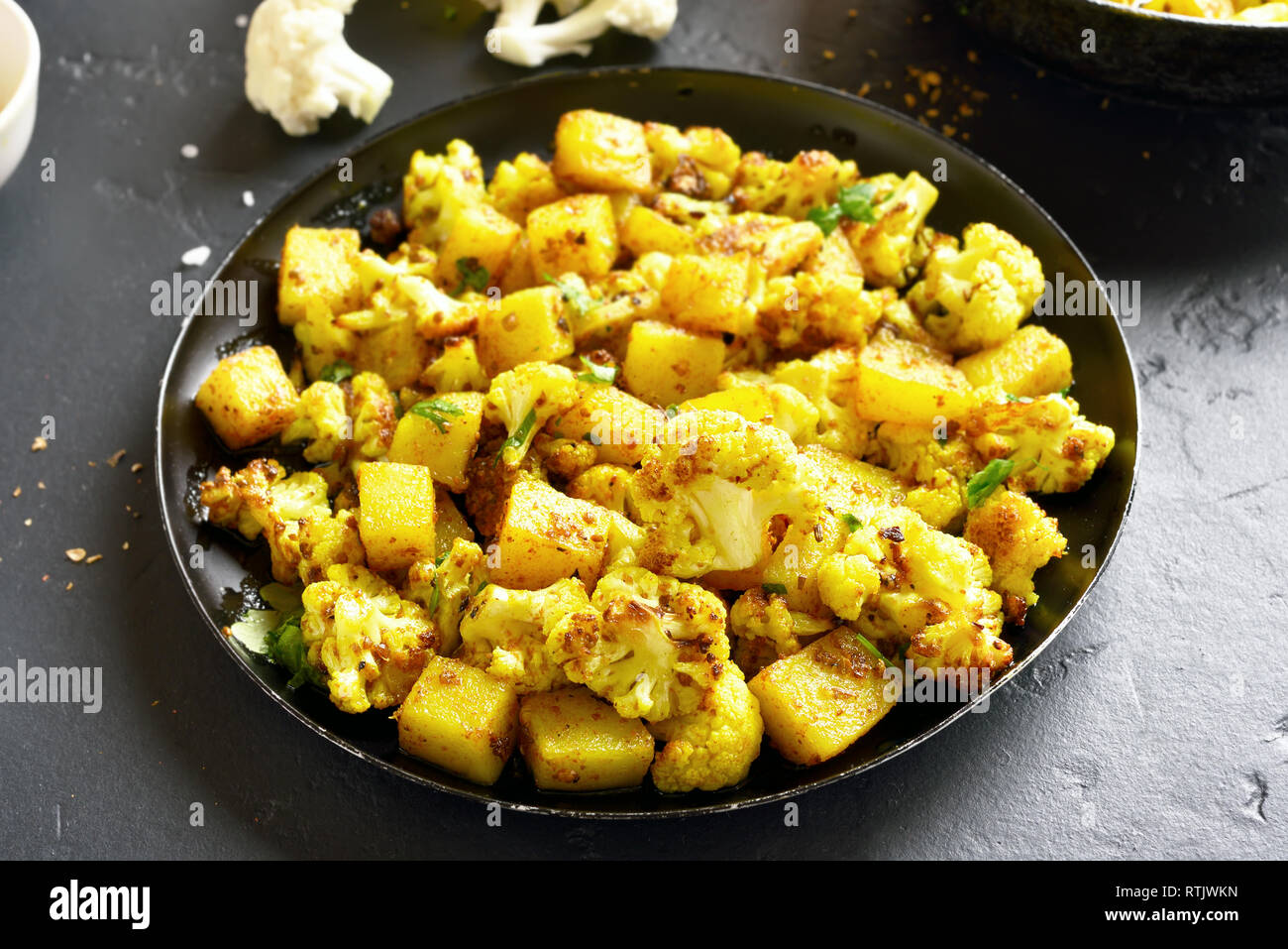 Nahaufnahme von Aloo Gobi indische Gericht. Gebratener Blumenkohl mit Kartoffeln in der Pfanne auf dem schwarzen Stein. Stockfoto