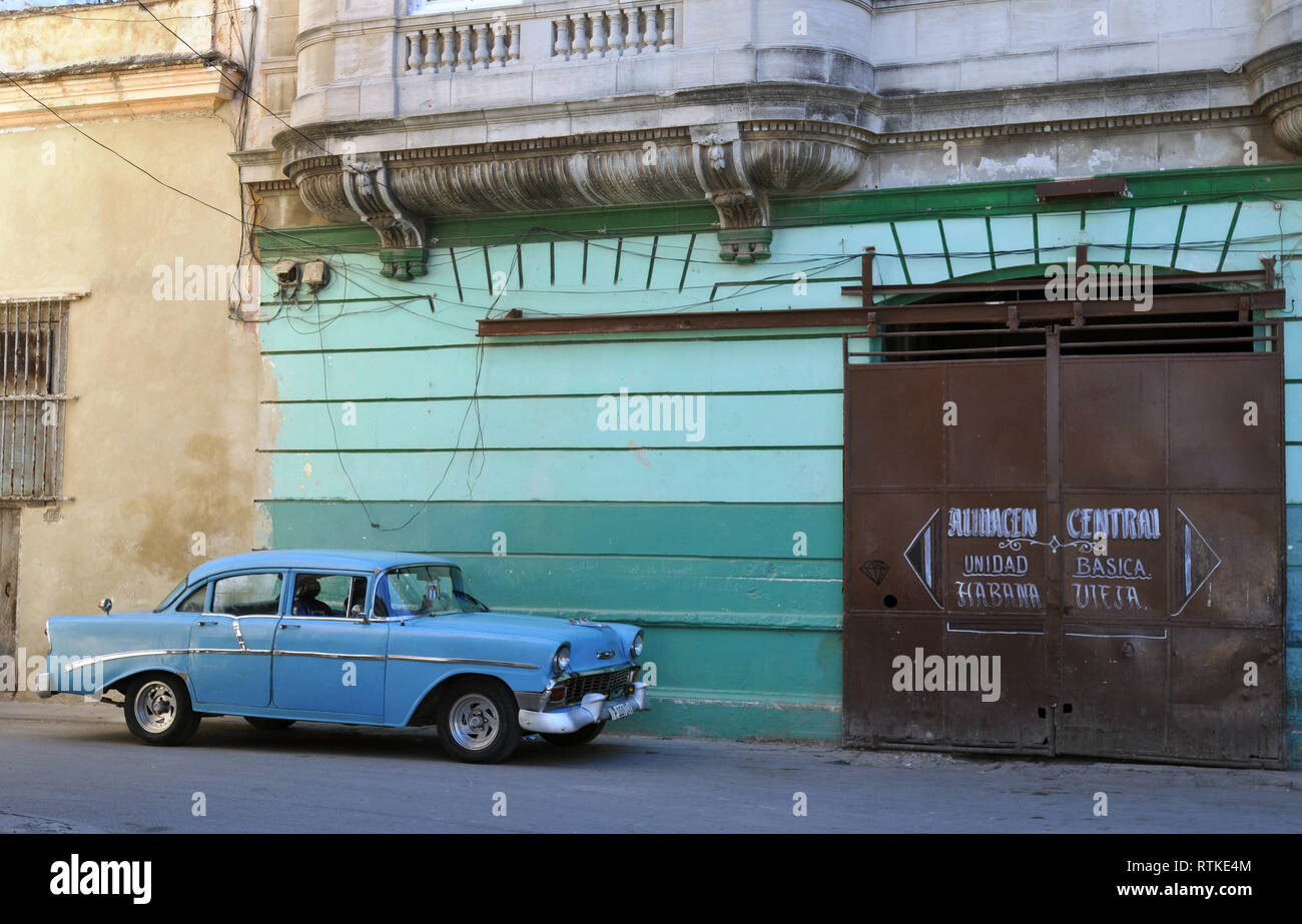 Straßenszene in Havanna, Kuba, zeigt ein klassisches blaues Auto vor einem Gebäude mit einem verschiebbaren Metall Tür geparkt auf einer gewölbten Eingang. Stockfoto