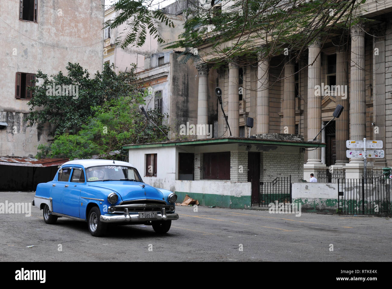 Ein klassisches blaues Auto sitzt auf einem Parkplatz in der Altstadt von Havanna, Kuba, in der Nähe von einem imposanten Gebäude mit hohen Säulen. Stockfoto