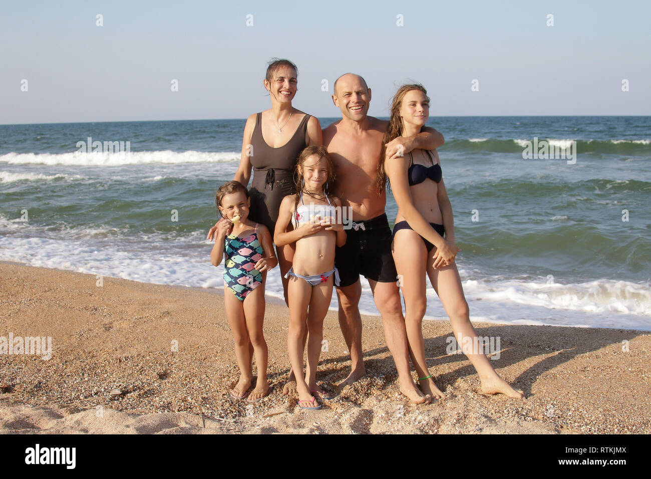 Gruppe Porträt einer gesunden Familie von 5 Personen, Mutter, Vater und drei Töchtern auf einem sonnigen Strand stehen auf dem Sand in Badekleidung und lächelnd wi Stockfoto