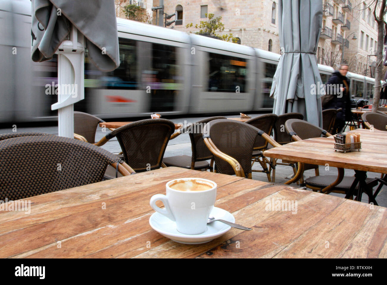 Eine Tasse Kaffee sitzt auf ein Café im Freien Tisch während der Jerusalem Light Rail durch Unschärfe im Hintergrund passiert. Stockfoto
