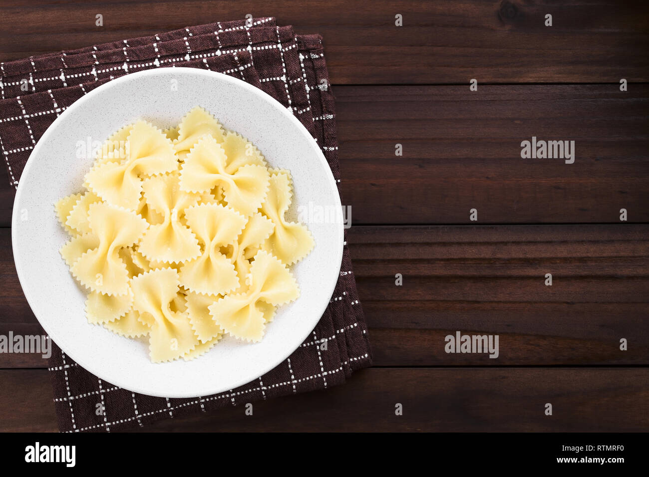 Frisch gekochte Farfalle, Bow-tie oder Schmetterling Pasta serviert in der Schüssel ohne Soße, mit copy space Overhead auf dunklem Holz fotografiert. Stockfoto