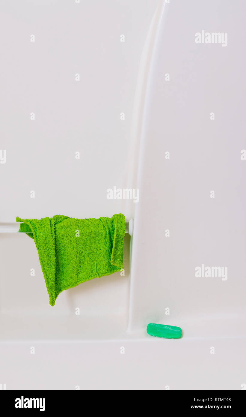 Vertikale Nahaufnahme der Mauer von einer Weißen Wanne. Grüne Waschlappen hängen von Handlauf und grüne Seife im Regal. Viele kopieren. Stockfoto