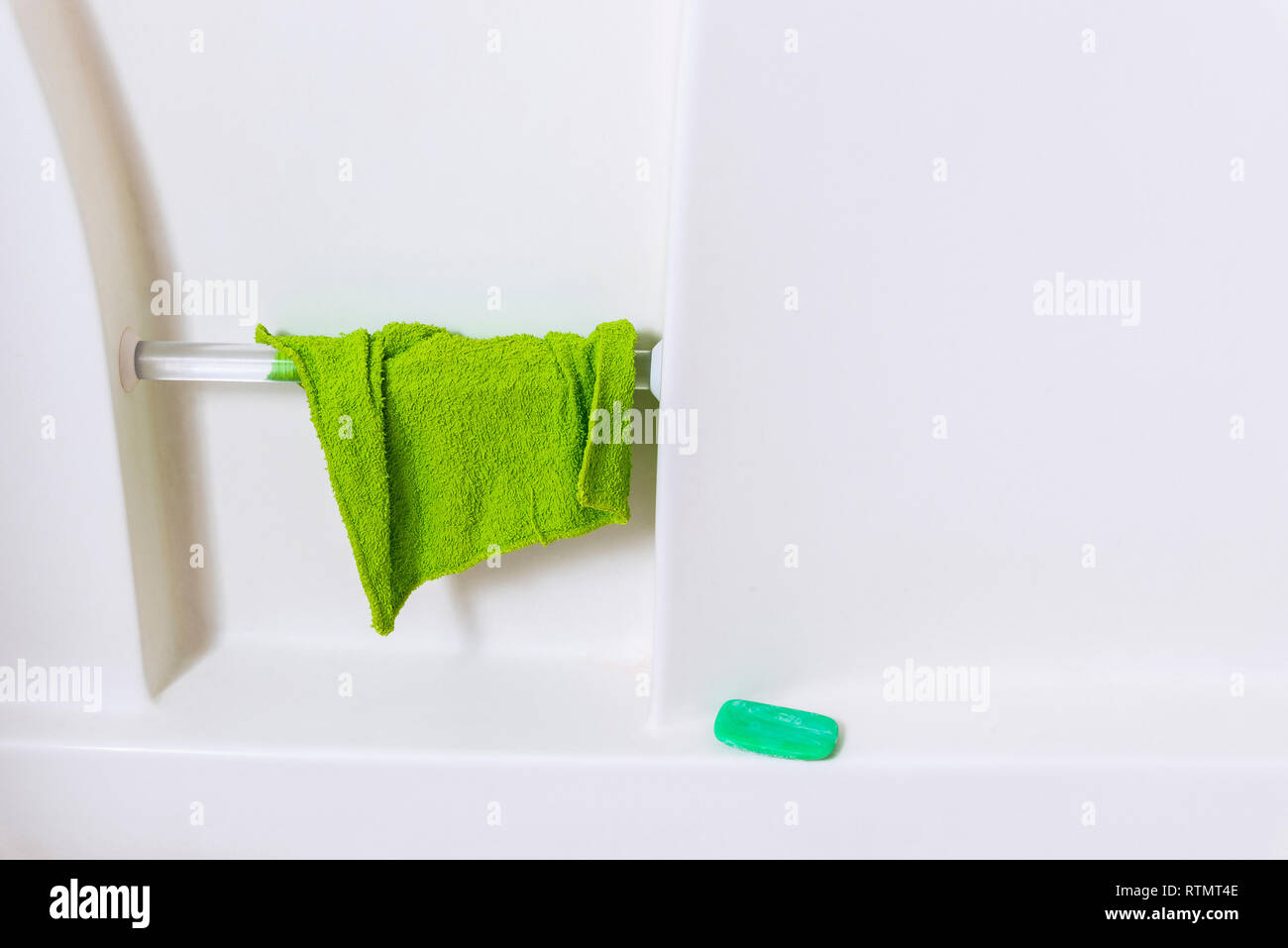 Horizontale Nahaufnahme der Mauer von einer Weißen Wanne. Grüne Waschlappen hängen von Handlauf und grüne Seife im Regal. Viele kopieren. Stockfoto