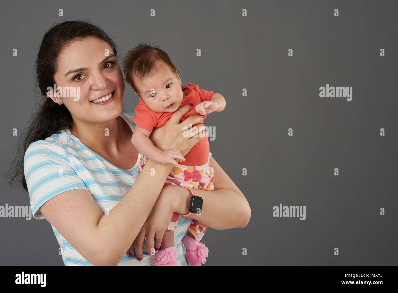 Glückliche junge Mama mit Baby in ungezwungener Atmosphäre auf grauem Hintergrund Stockfoto