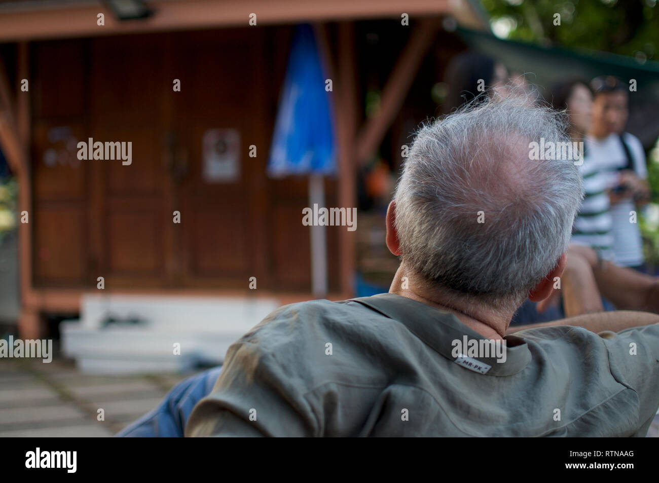 BANGKOK, THAILAND - 11. Dezember 2018: Heck Bild von einem Mann auf einer Bank sitzen, während er auf der Suche ist, Menschen zu Fuß am Wat Arun, Bangkok, Thailand Stockfoto