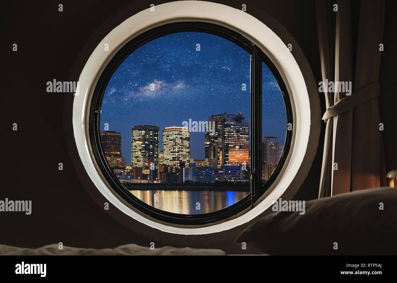 Runde Fenster im Schlafzimmer bei Nacht mit Blick auf die Stadt Stockfoto