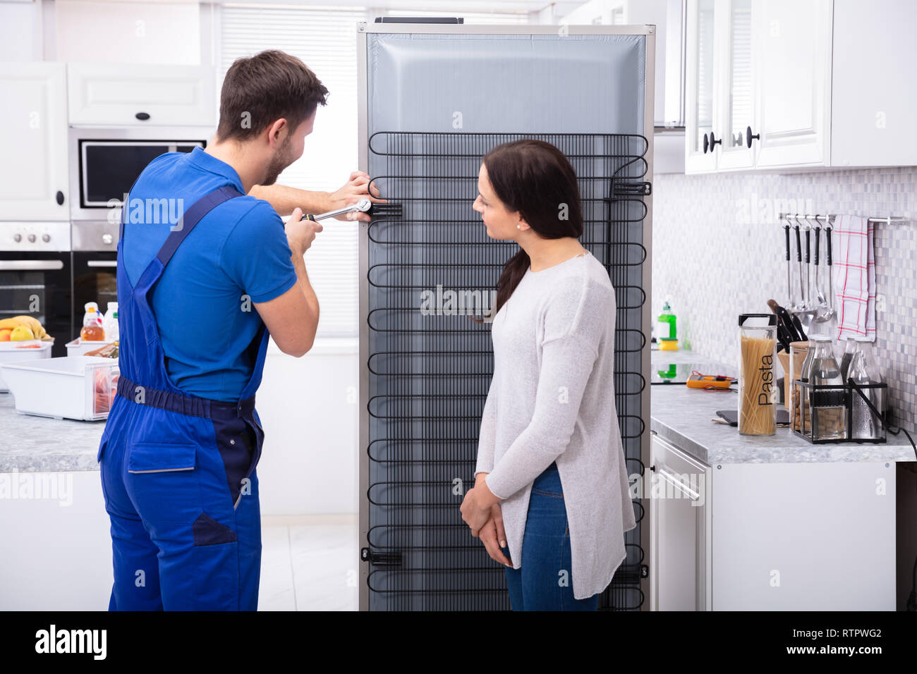 Frau an Techniker Reparatur Kühlschrank mit Schraubendreher in der Küche auf der Suche Stockfoto