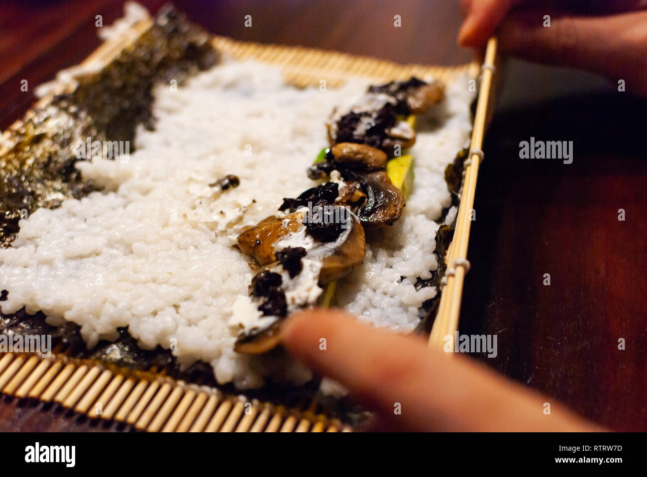 Seitenansicht eines jungen Frauen rolling Hausgemachte vegane Sushi auf einem Holztisch Stockfoto