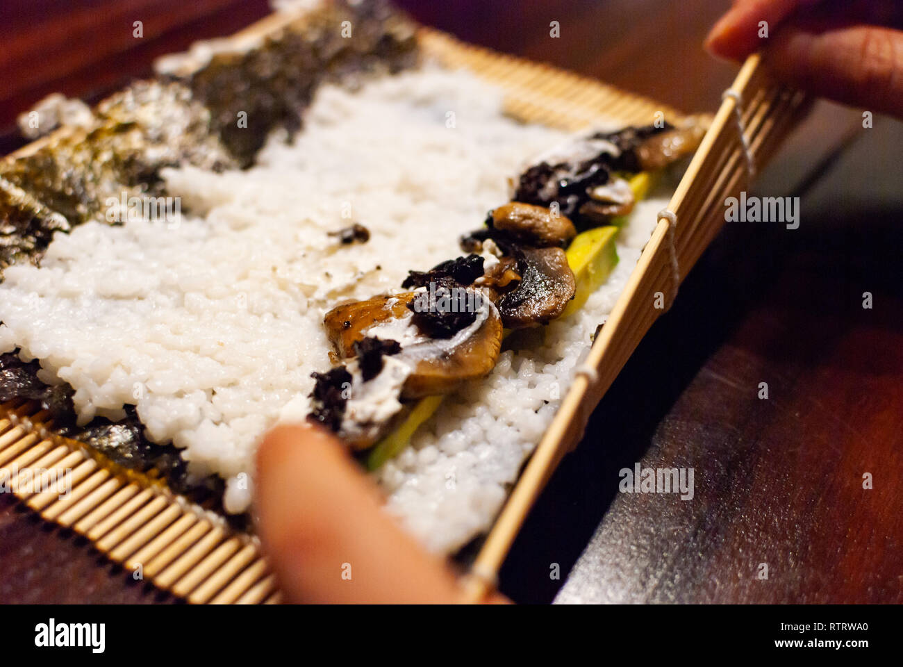 Seitenansicht eines jungen Frauen rolling Hausgemachte vegane Sushi auf einem Holztisch Stockfoto