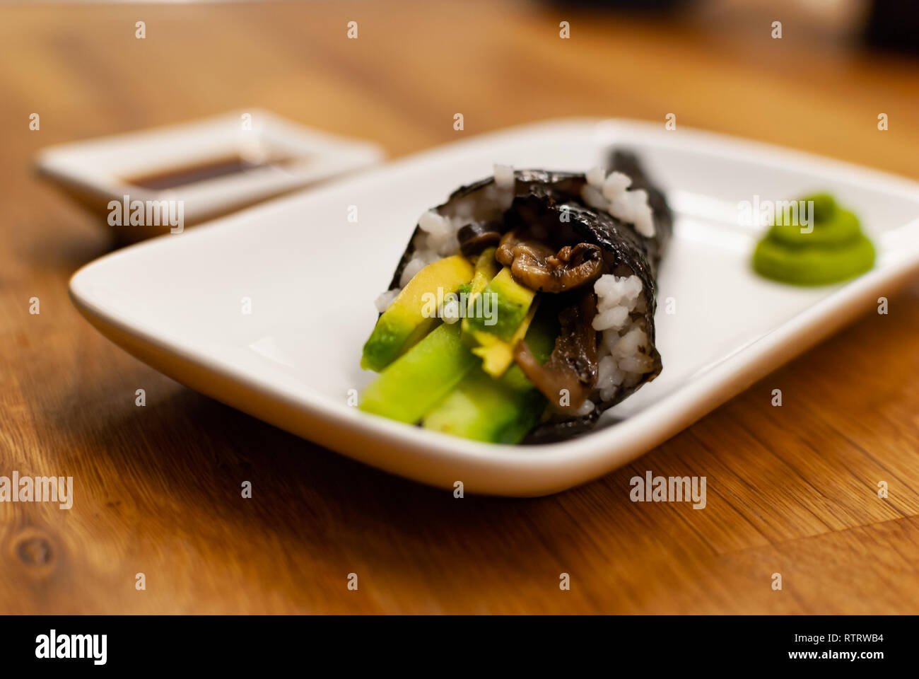 Seitenansicht Seitenansicht mit hausgemachten vegan Temaki-Sushi mit Avocado auf einen kleinen Teller gefüllt auf einem Holztisch mit Sojasauce und Wasabi Stockfoto