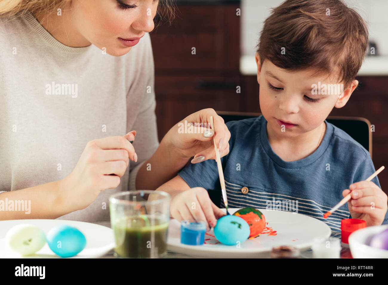 Junge schöne blonde Mutter und ihre niedlichen vier Jahre alten Sohn Spaß beim Malen Eier zu Ostern zu Hause Küche, lächelnd, Entwicklung kreativer Ein Stockfoto