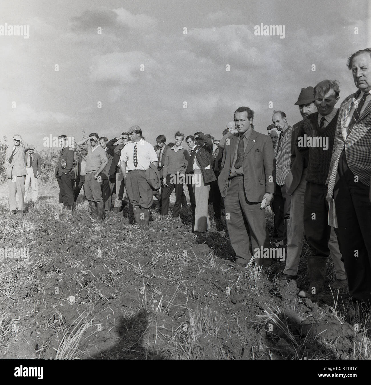 1967, Country Life..... Beamten und örtlichen spectactors stehend in den Furchen des Feldes auf dem Bauernhof gerade eine junge Landwirte pflügen übereinstimmen, England, UK. Stockfoto