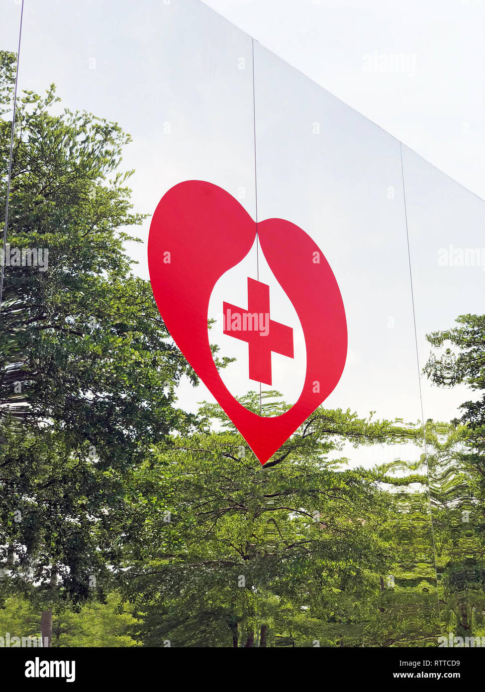 Rotes Herz und Rotes Kreuz auf sich Metall Wand und Bäume im Hintergrund Stockfoto