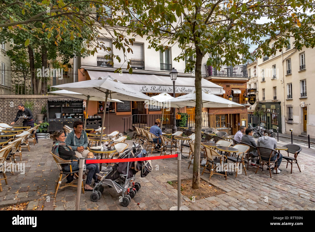Ein Paar mit einem Baby Entspannen an einen Tisch draußen Restaurant Le Relais De La Butte, während ein Kellner nimmt einen Auftrag, ein Restaurant in Montmartre, Paris Stockfoto