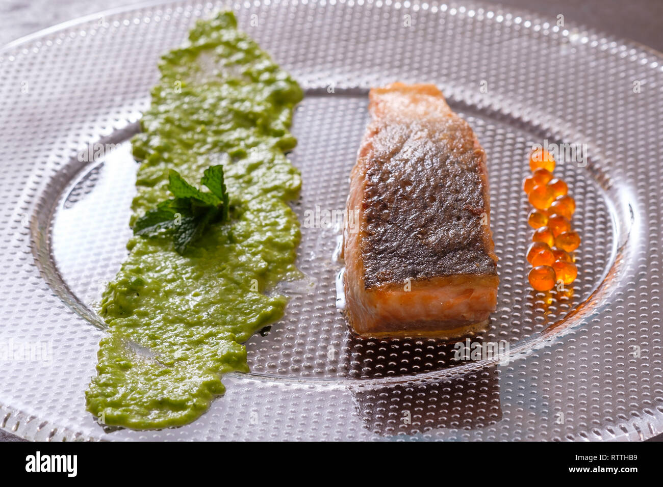 Gebratener Lachs Fisch mit Haut und Erbsenpüree und Kaviar in der Hintergrundbeleuchtung Stockfoto