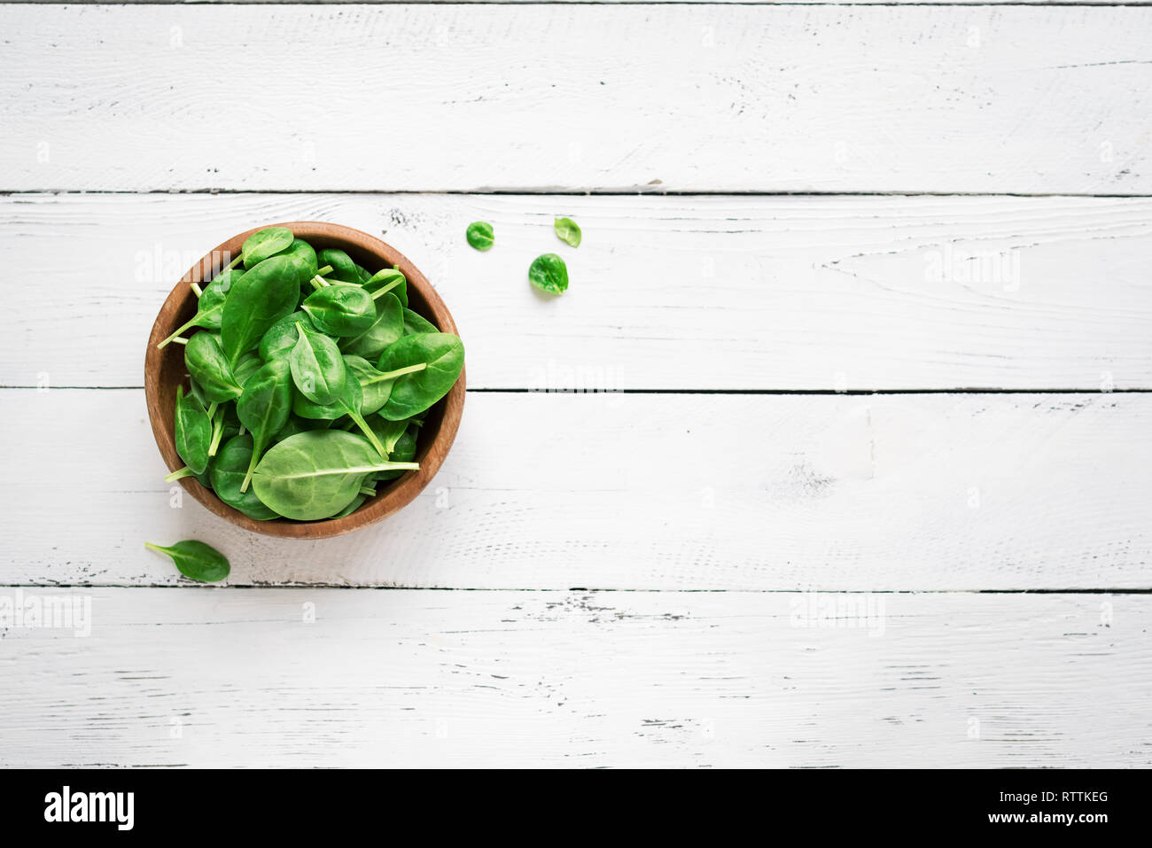 Baby Spinatblätter in der Schüssel auf weißem Holz- Hintergrund, Ansicht von oben, kopieren. Sauber Essen, Detox, Diät Lebensmittel Zutat - grün Bio Spinat. Stockfoto