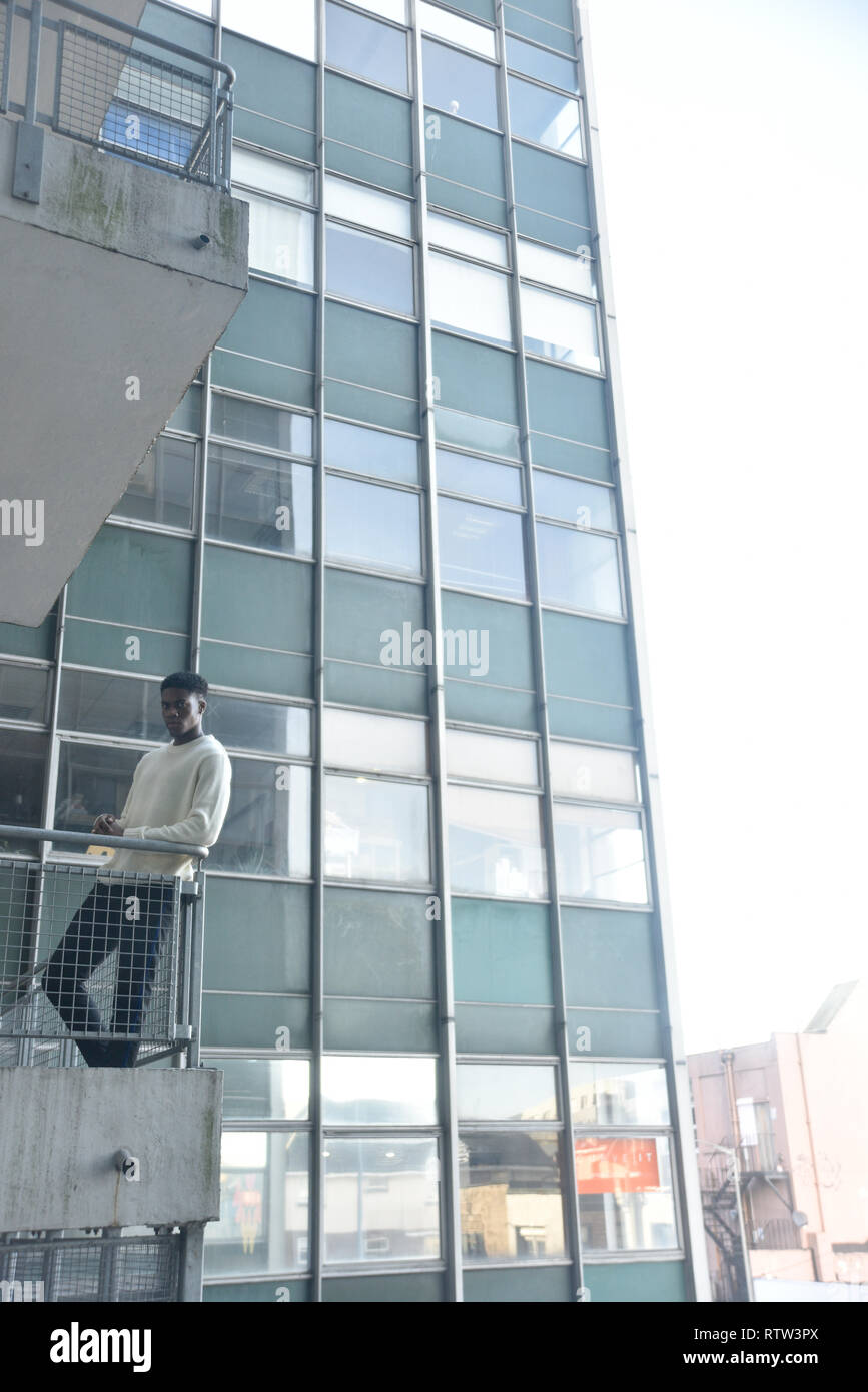Porträt von einem gutaussehenden jungen männlichen Schwarzen ständigen Alon auf eine Treppe gut zu einem Hochhaus in der Stadt Lage - Er sieht ernste und traurige Stockfoto