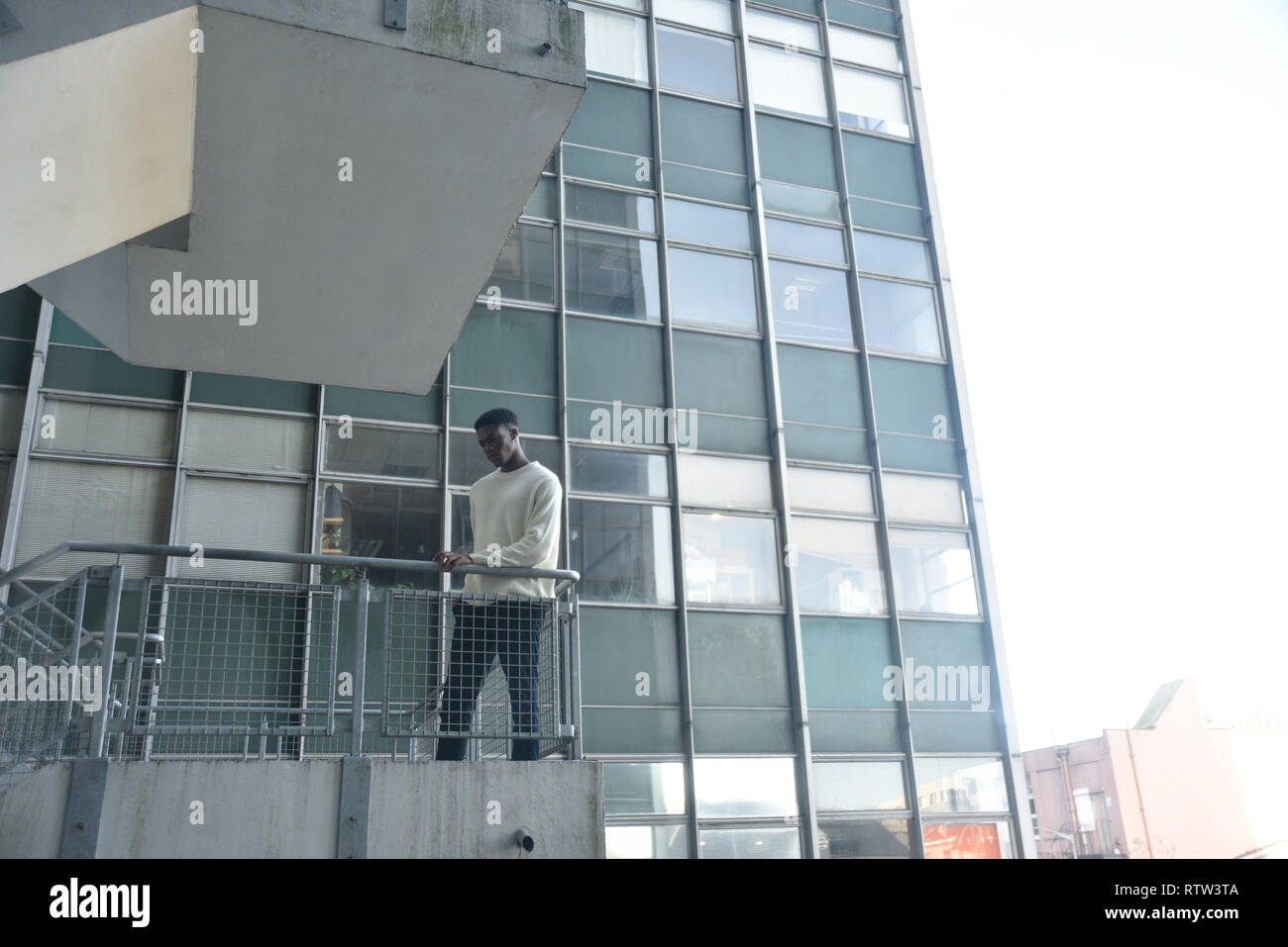 Porträt von einem gutaussehenden jungen männlichen Schwarzen ständigen Alon auf eine Treppe gut zu einem Hochhaus in der Stadt Lage - Er sieht ernste und traurige Stockfoto