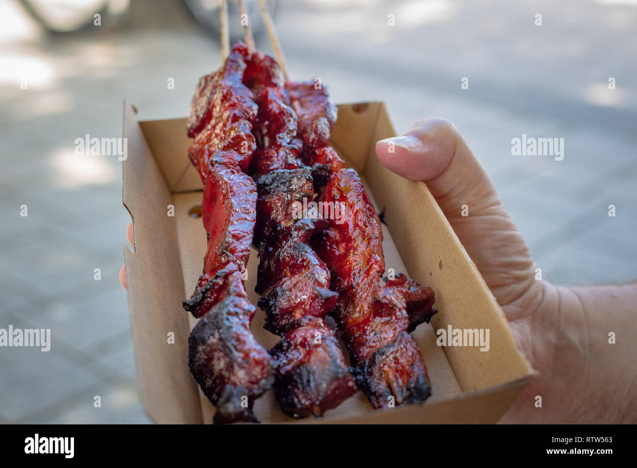 Ein Mann kauft köstlich marinierte gegrillte Fleischspieße in einem Karton biologisch abbaubar Takeaway Behälter an einem Lebensmittelmarkt in Christchurch, Neuseeland Stockfoto