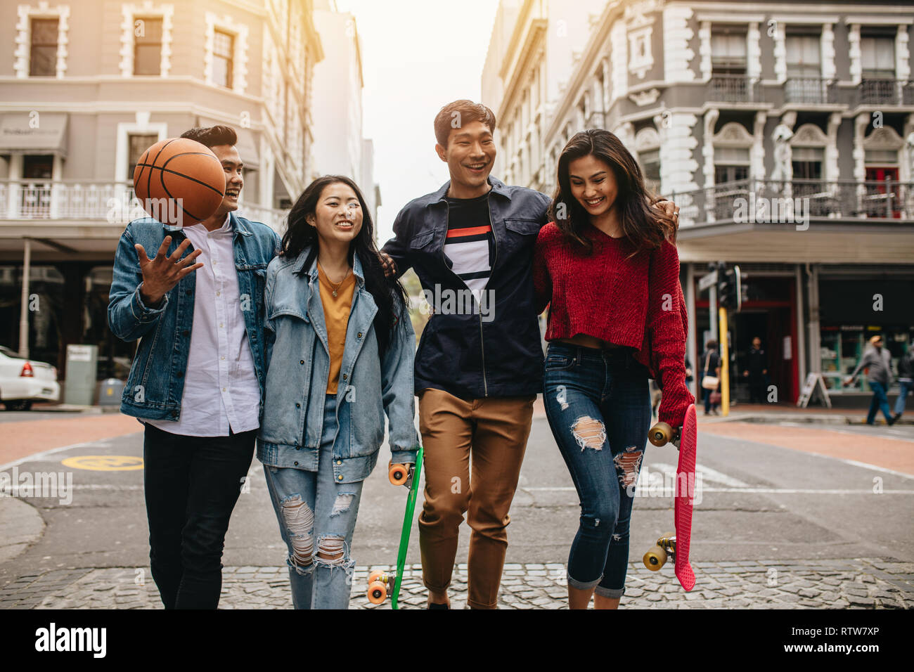 Gruppe von asiatischen Frauen und Männer wandern im Freien mit Skateboard und Basketball. Vier Freunde gehen auf die Straße der Stadt. Stockfoto
