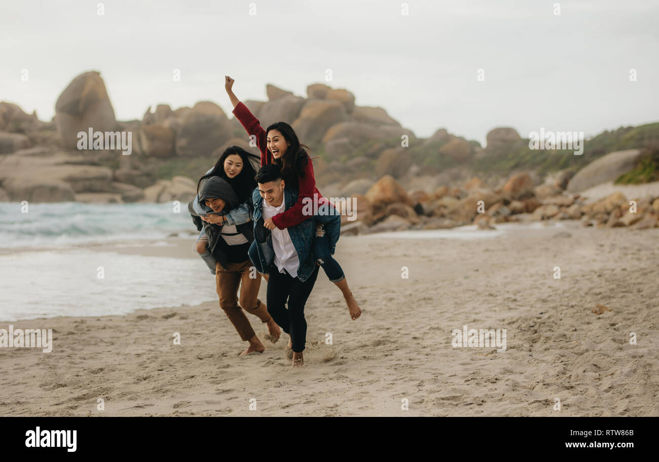 Zwei junge Männer, die ihre Freundinnen piggyback Rides. Gruppe junger Leute genießen, sich im Sommer am Strand. Stockfoto