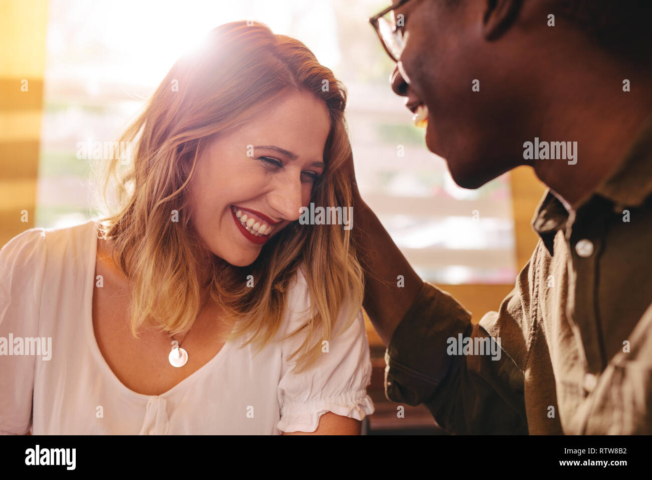 Lächelnde Frau am Tag mit ihren liebevollen Freund im Cafe. Mixed Race Paar zusammen. Im Café sitzen mit hellem Sonnenlicht zurück. Stockfoto