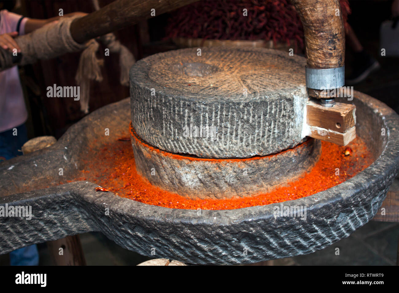 Mahlen Getrocknete rote Chilis von Hand in einer Steinmühle. Gemahlener roter Chili Pulver. Stockfoto