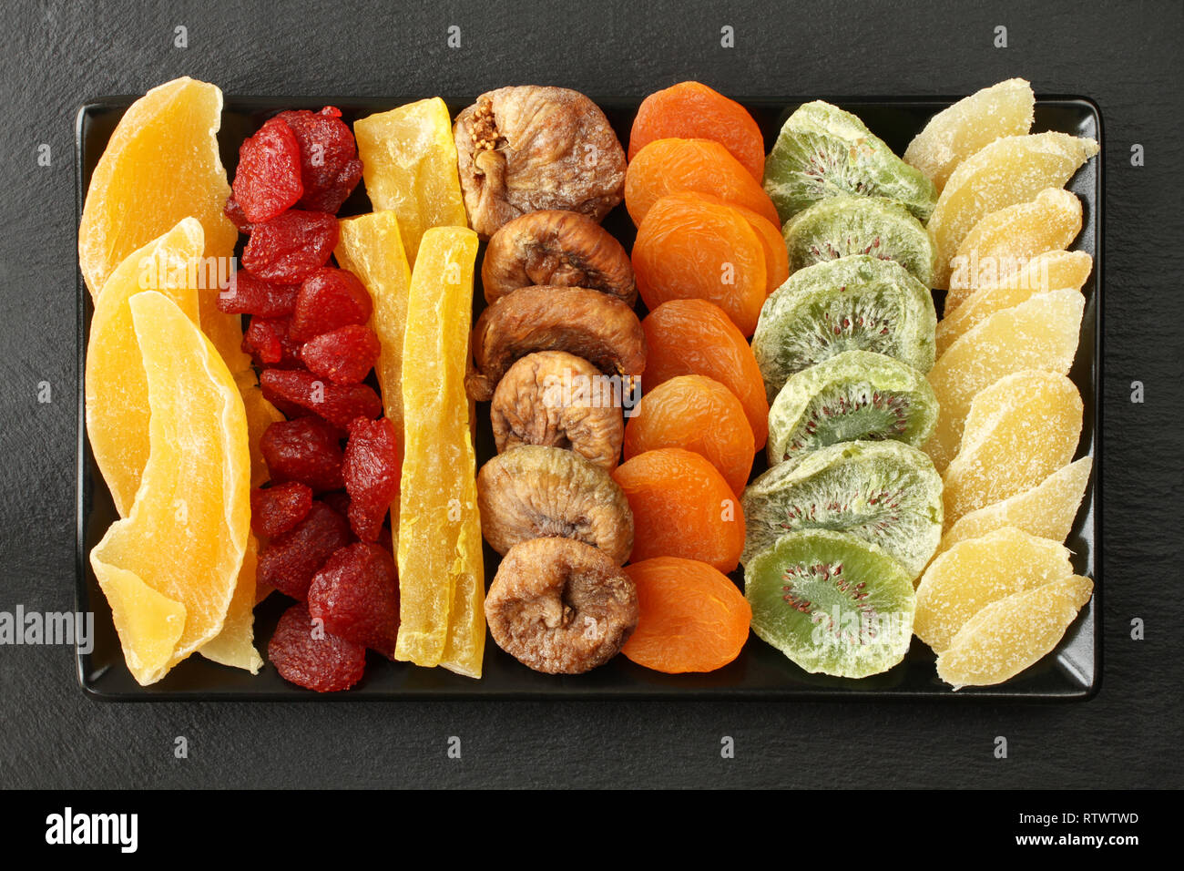 Trockenfrüchte Mango, Papaya, Kiwi, getrocknete Erdbeeren, Feigen, Aprikosen Stücke kandierten Ingwer Wurzel, der lag auf einem schwarzen Keramikplatte auf einem blac Stockfoto