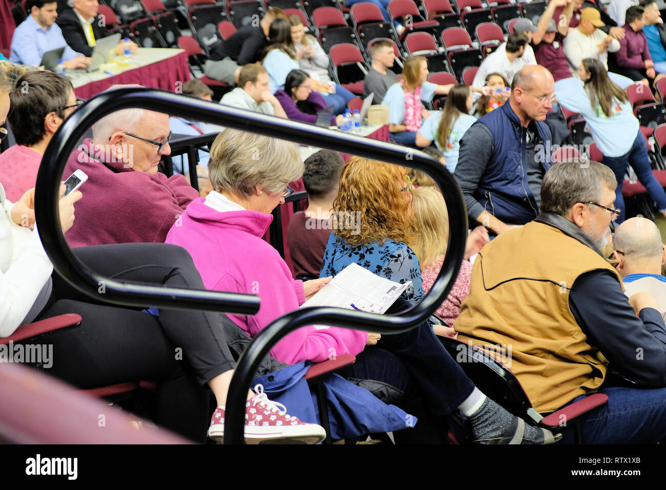 Frau Lösung Kreuzworträtsel an einem Basketballspiel; Mann über die Schulter schauen; Langeweile; langweiliges Spiel, langweilige Unterhaltung. Stockfoto