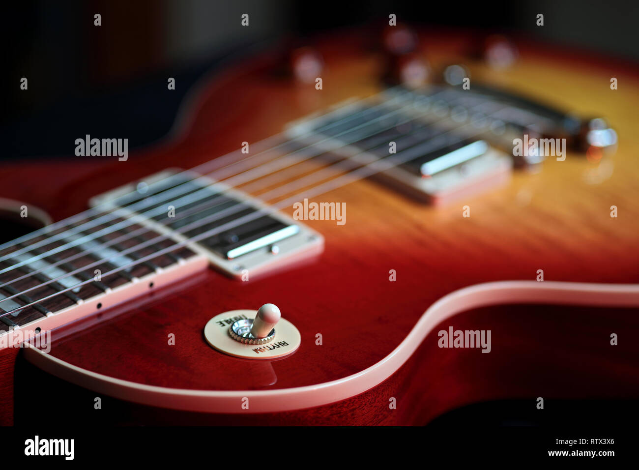 Nahaufnahme des Rhythmus und Höhen Switch auf einer neuen Cherry Red E-Gitarre mit Streichern im Hintergrund Stockfoto