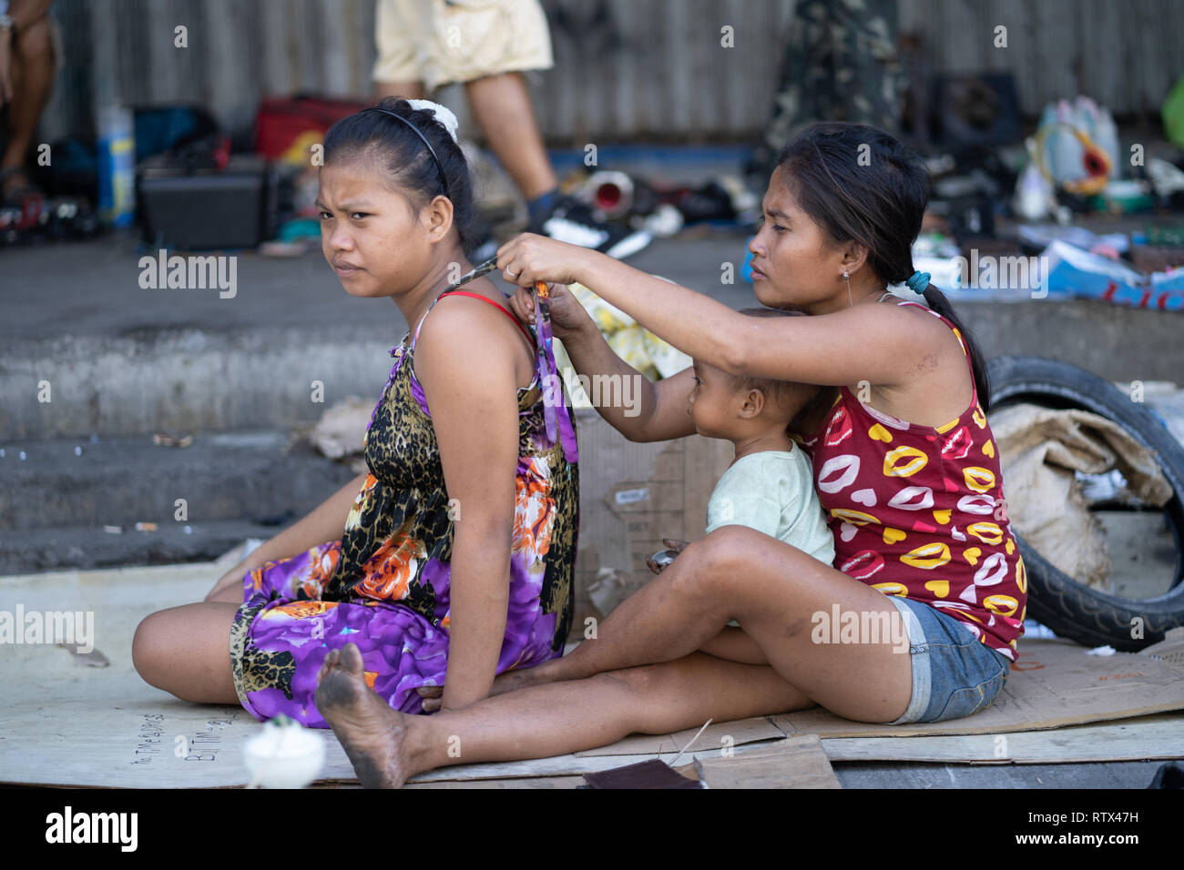 Zwei philippinische Frauen, ohne Schuhe, und ein Kind sitzen auf Karton in einer Seitenstraße, Cebu City, Philippinen Stockfoto