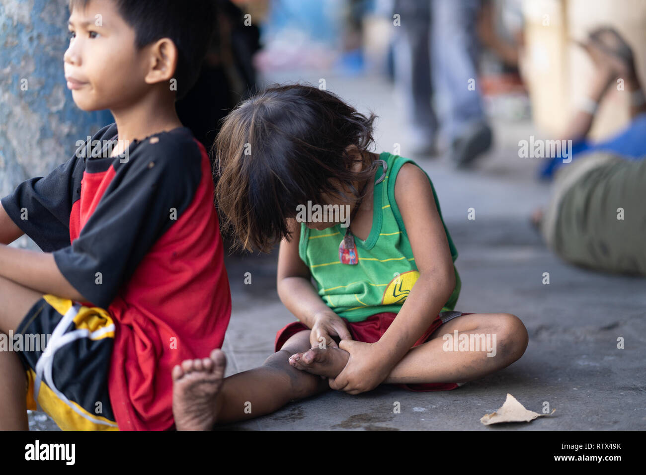 Ein Kind ohne Schuhe sitzen auf einem Bürgersteig in Cebu City, Philippinen Stockfoto