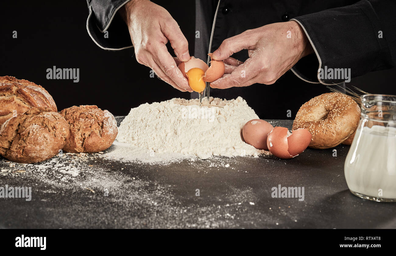 Baker Aufschlagen der Eier in einem Haufen backen Mehl mit Milch in einem Krug, als er seine Spezialität Brot bereitet Stockfoto