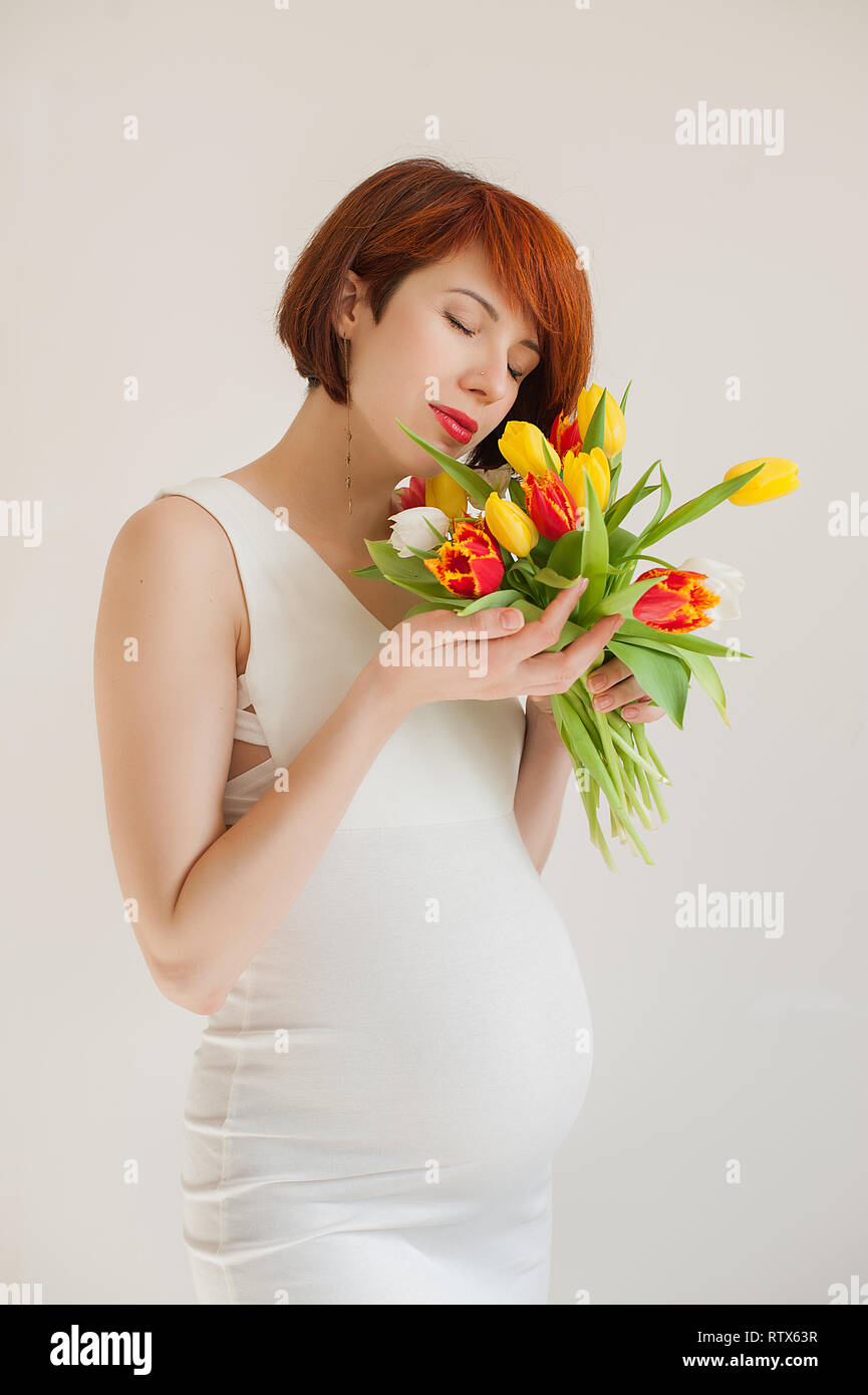 Glückliche junge schwangere Frau in weißem Kleid mit Blumen Stockfoto