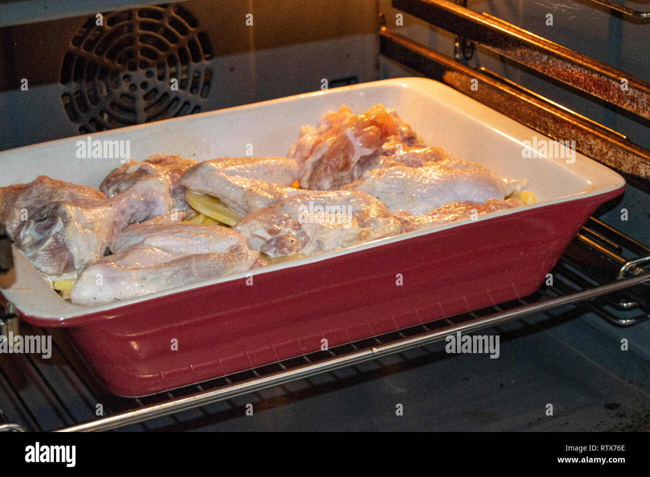 Leckere hausgemachte Braten mit Huhn und Kartoffeln, rohe Zutaten in einem keramischen Pfanne im heißen Ofen ein Abendessen mit der Familie Stockfoto
