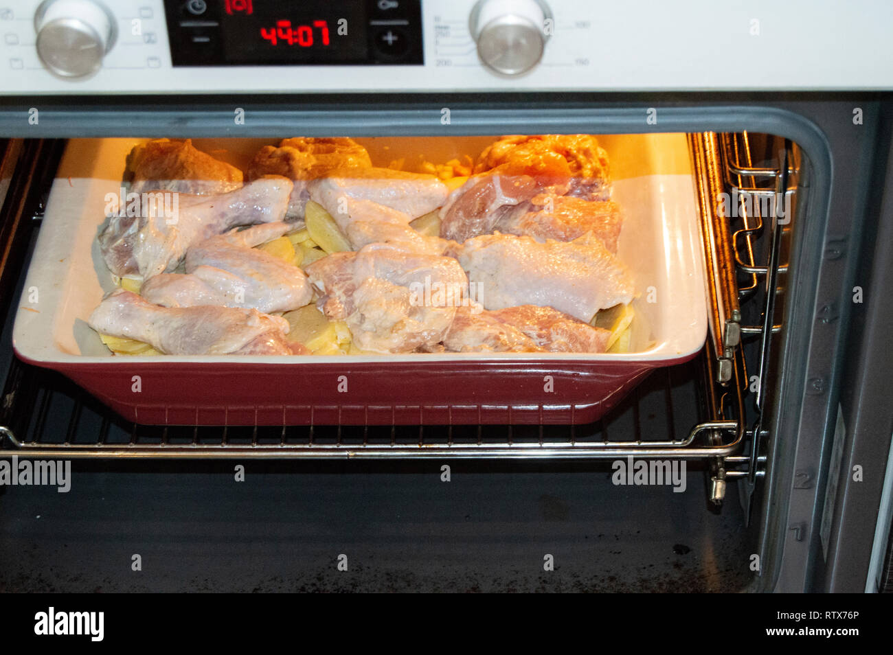 Leckere hausgemachte Braten mit Huhn und Kartoffeln, rohe Zutaten in einem keramischen Pfanne im heißen Ofen ein Abendessen mit der Familie Stockfoto