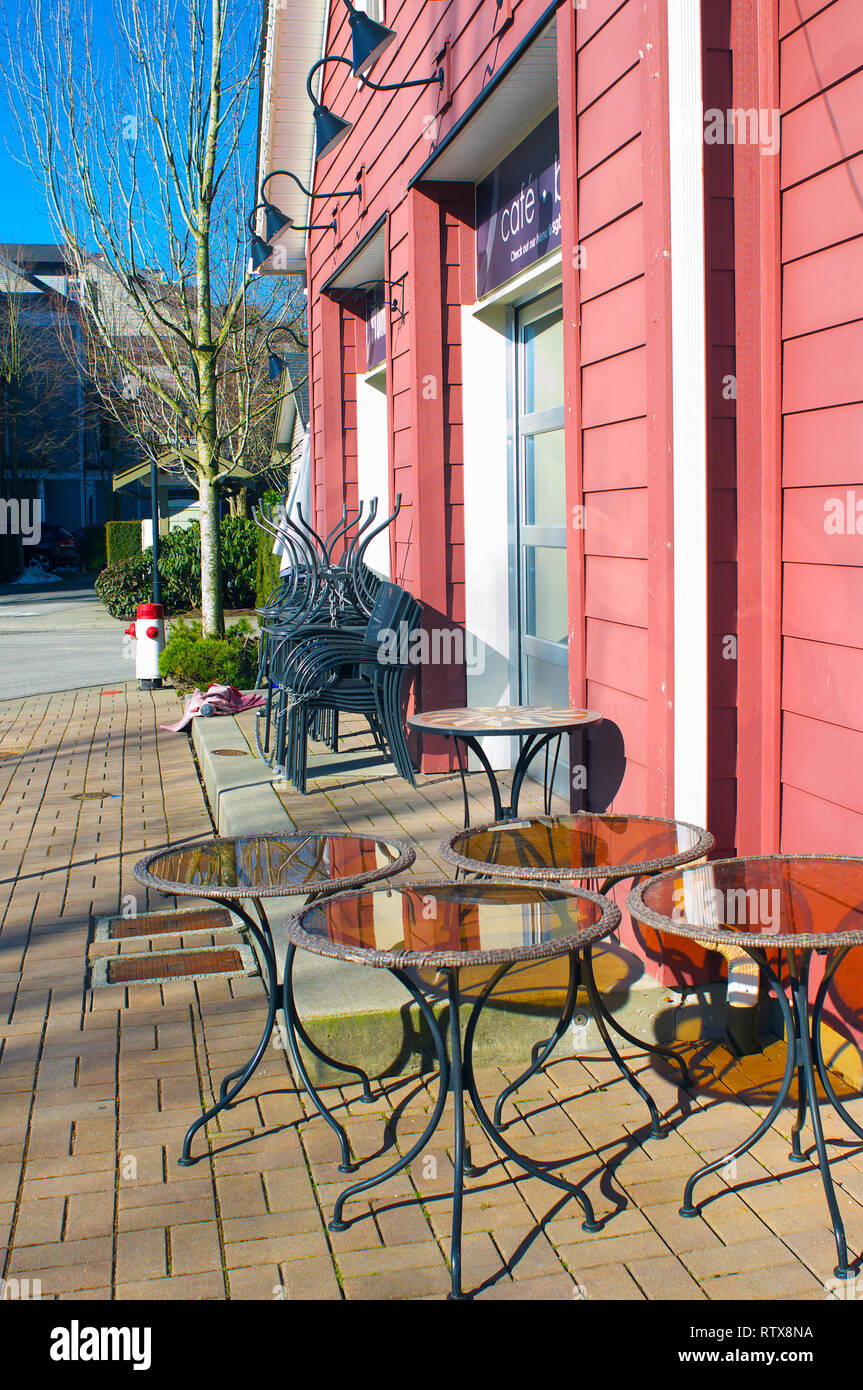 Seitenansicht des Gebäudes mit Tischen im Freien und gestapelte Stühle auf der Terrasse. Stockfoto