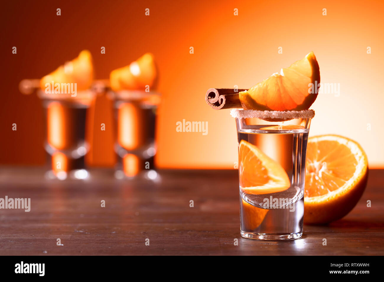 Gläser tequila mit Orangenscheiben und Zimtstangen auf einem Holztisch. Stockfoto