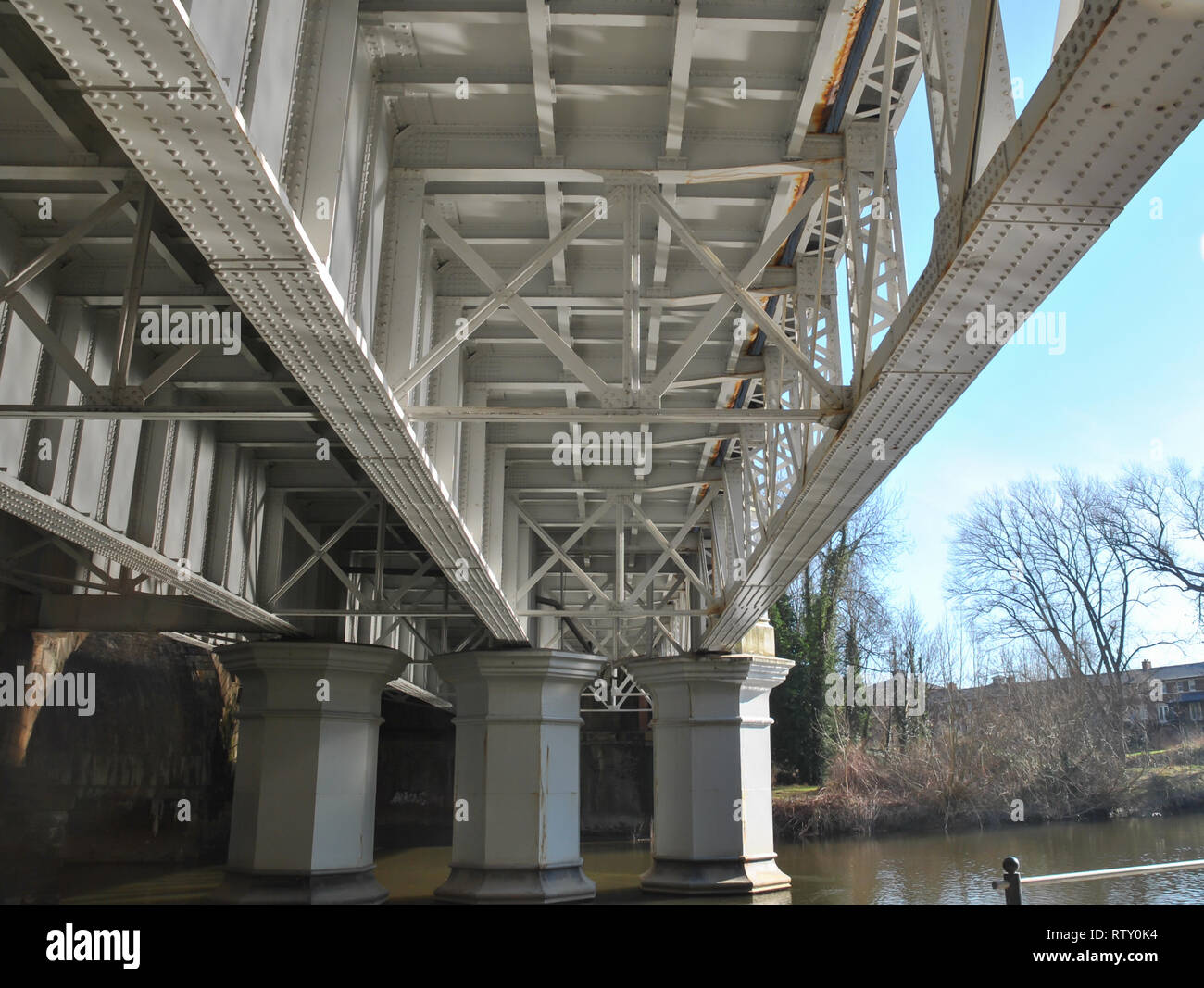 Die Unterseite einer Eisenbahnbrücke, Stahl, bei Lattice von Balken mit Sonnenlicht back up aus dem Fluss Stockfoto