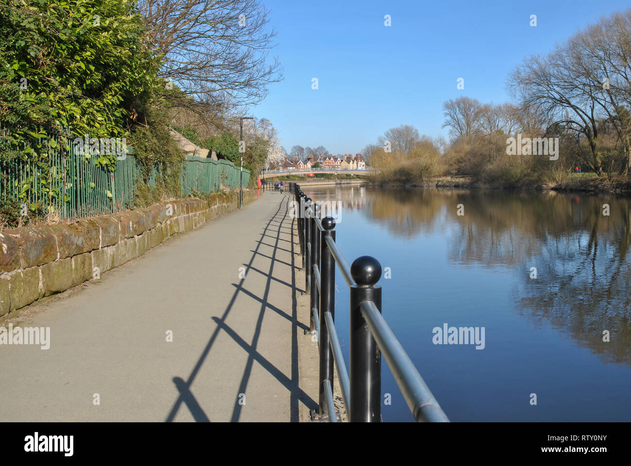 Geländer entlang des Flusses in Shrewsbury zeigt starke Schatten auf dem Weg und einem klaren blauen Himmel Stockfoto