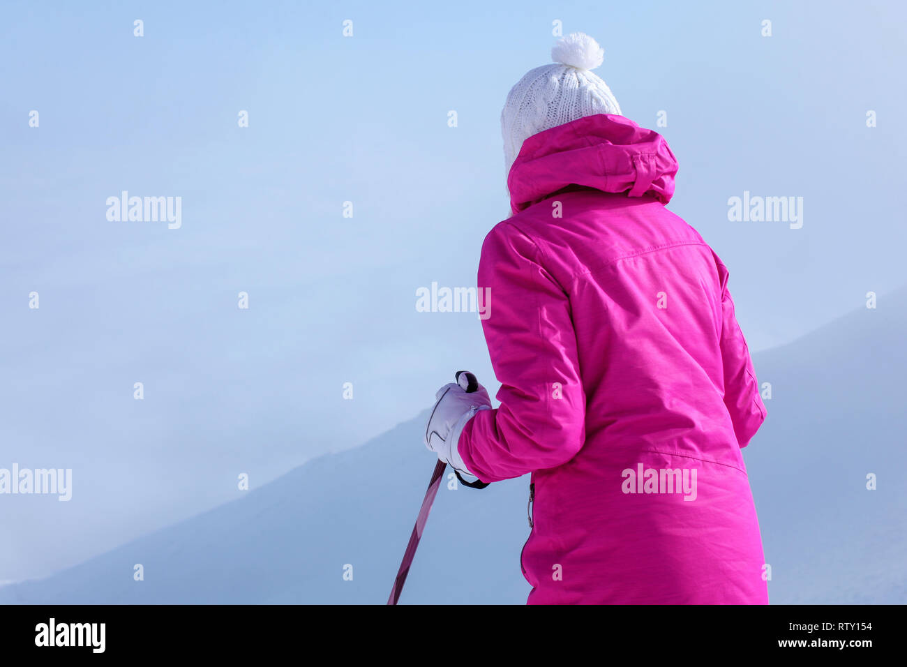 Von hinten betrachten, junge Frau in rosa Winterjacke, Stöcke in die Hände, um den Hügel hinunter zu gehen. Stockfoto