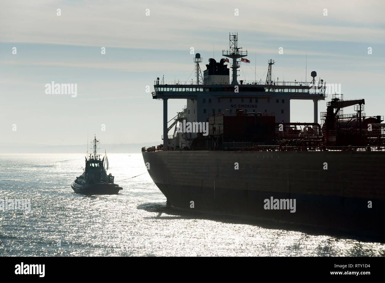 Southampton, Hampshire, England, UK. Februar 2019. Am frühen Morgen gegen das Licht geschossen von einem Schlepper in Anwesenheit einer breiten Strahl Öltanker o Stockfoto