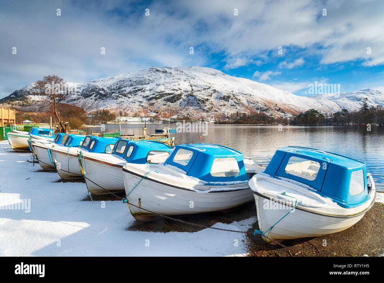 Eine Reihe von Booten auf dem verschneiten Ufer von Ullswater in Glenridding im Nationalpark Lake District in Cumbria Stockfoto