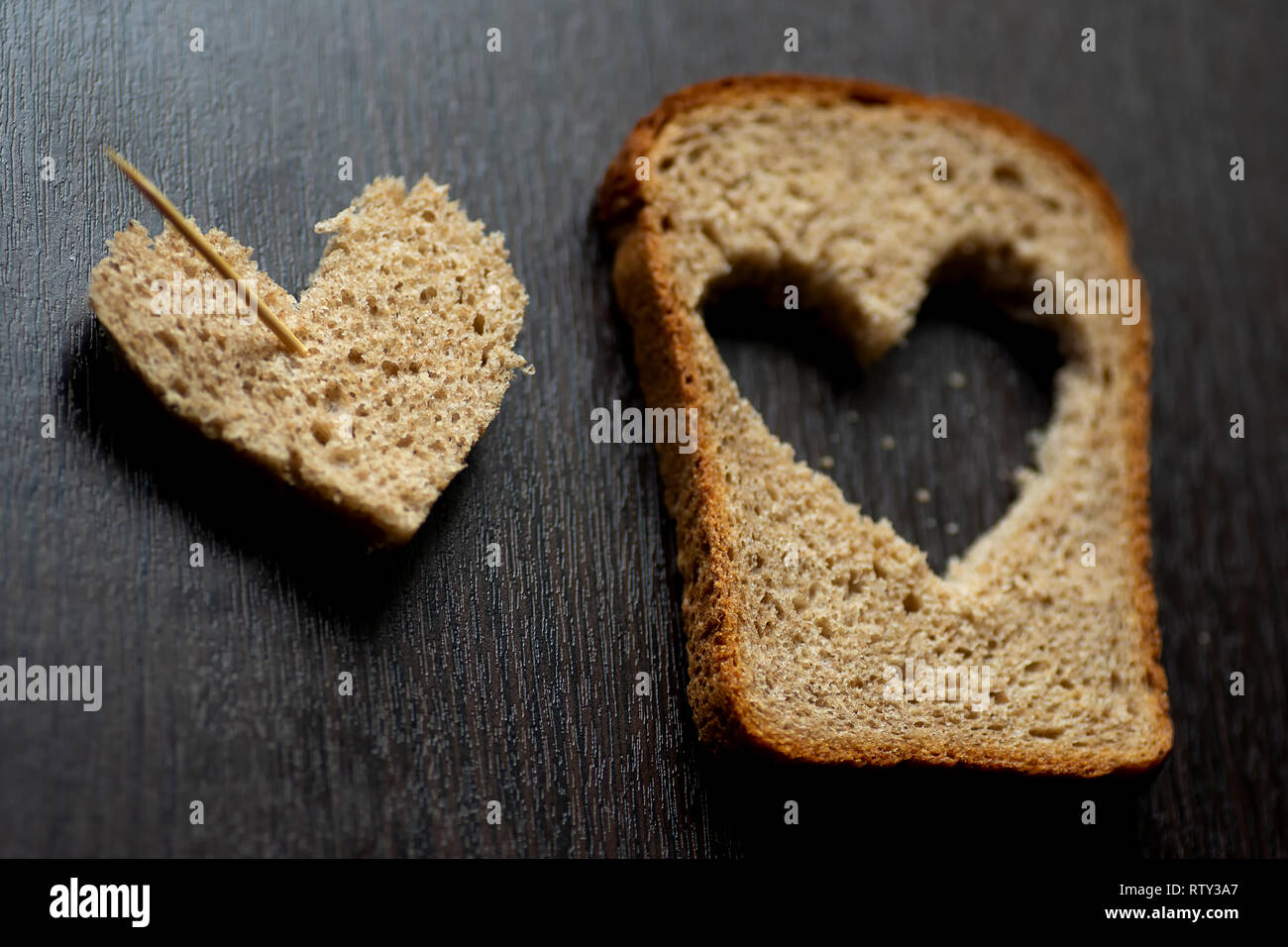 Herzen geschnitzt aus einem Stück Brot auf einem dunklen Holztisch Stockfoto