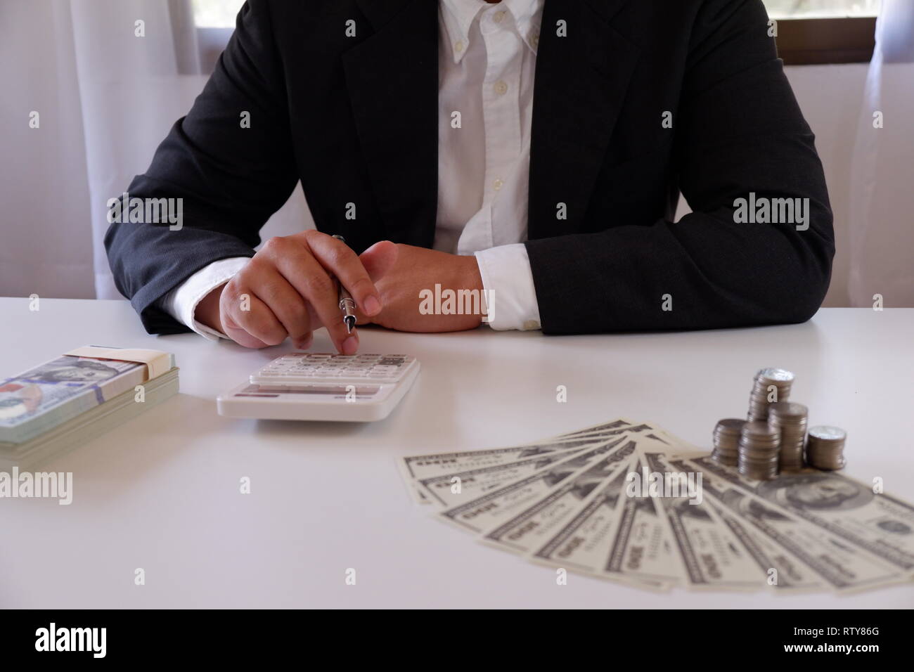 Geschäftsmann mit Taschenrechner mit Münzen und Geld über den Schreibtisch Stockfoto