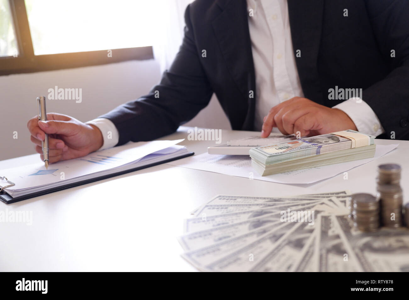 Geschäftsmann mit Taschenrechner mit Geld und Stapel von Münzen auf dem Schreibtisch Stockfoto