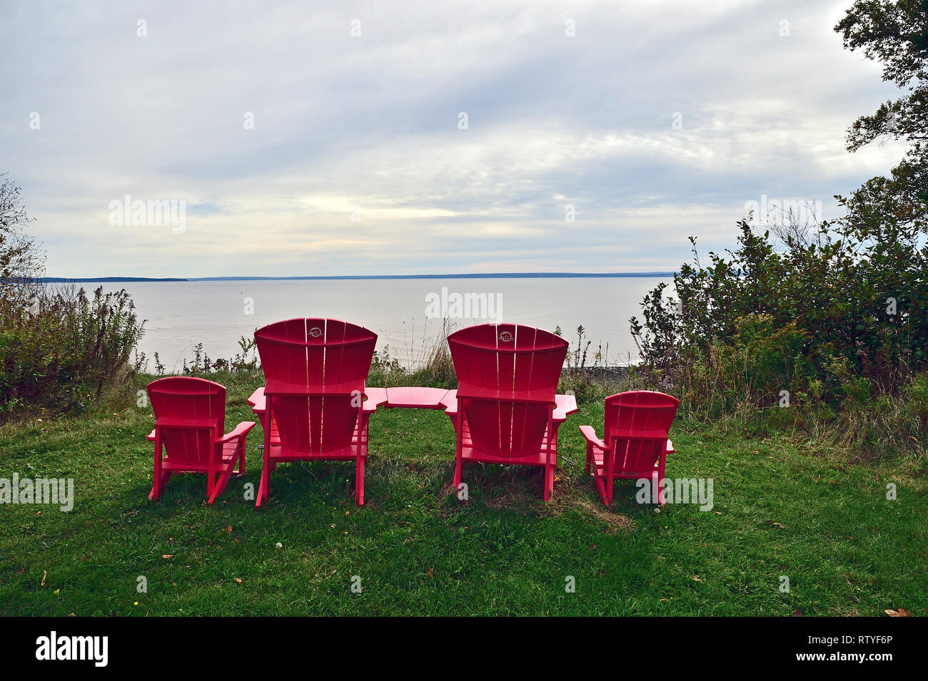 Vier rote Holzstühle sitzen zusammen an einem Aussichtspunkt mit Blick über das Wasser der Bay of Fundy im Fundy National Park New Brunswick Canada. Stockfoto