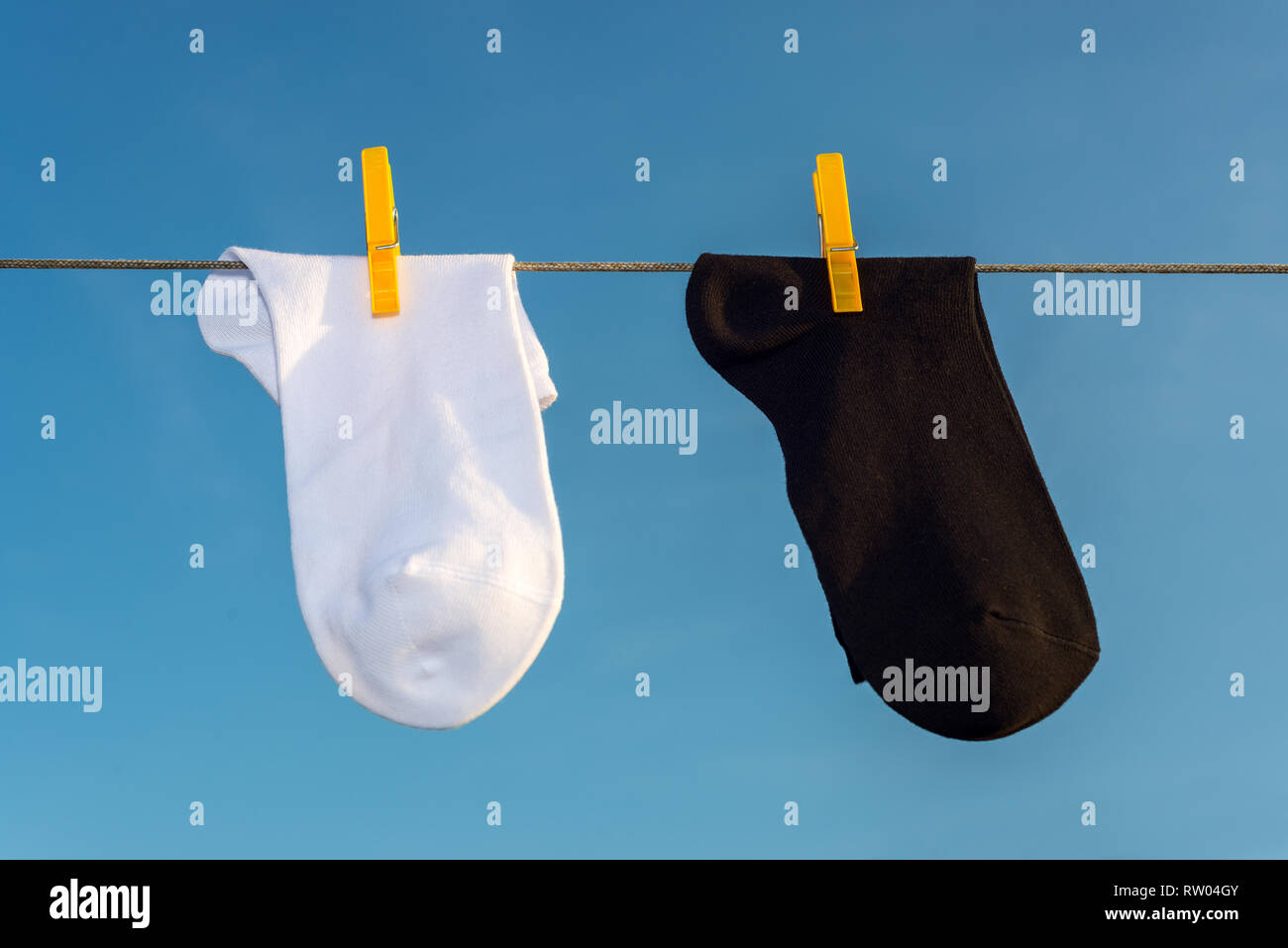 Zwei neue, saubere, gewaschene schwarze und weiße Socken hängen an einem Seil mit gelben Wäscheklammern. und blauer Himmel Stockfoto